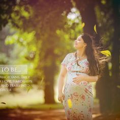 a pregnant woman standing in the woods with her hands on her hips and looking up into the sky