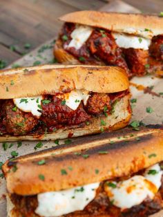 three meatball sub sandwiches with sauce and sour cream on them sitting on a piece of parchment paper