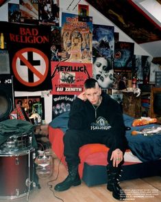 a man sitting on top of a bed in a room filled with posters and drums