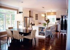 an open kitchen and dining room area with hardwood flooring, stainless steel appliances and large windows