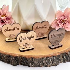 three wooden hearts with names on them sitting on top of a piece of wood next to flowers