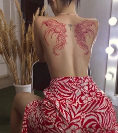 a woman sitting in front of a mirror wearing a red dress with dragon tattoos on her back