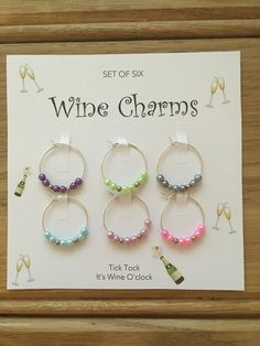 six wine charms in different colors and sizes are displayed on a wooden table with a sign