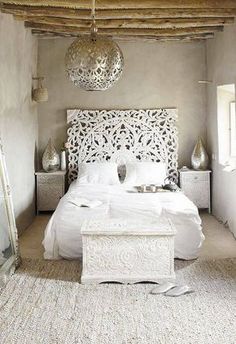 a white bed sitting in a bedroom next to a wooden table and lamp hanging from the ceiling