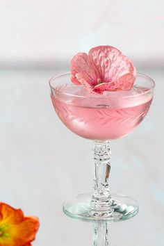 a pink drink in a wine glass with a flower on the rim next to it