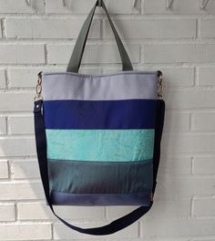 "Vibrant large canvas tote bag with stripes of different fabrics in shades of blue and grey in a slightly trapezoidal silhouette.  With its large capacity, adjustable shoulder strap and short handles, it's perfect for carrying everything you need to enjoy a stroll, a day at the beach or shopping on your summer or mid-season days. With its playful and versatile striped design, it's easy to match with a variety of outfits.  A basic that will always be with us. Materials: * Outside: Canvas, Cotton, Wild silk, Polyester upholstery * Lining:  Cotton satin (cotton/polyamide) * Padding: foam stabilizer, interfacing fabric. * Strap: nylon * Zipper: nylon   Zipper puller: faux suede leather cord  * Gold metal hardware  Approx. measures: Width:   31 cm ( 12,20 \") Height:  33 cm ( 13 \")  Depth: Interfacing Fabric, Canvas Shopper Bag, Fabric Handbags, Fabric Strap, Blue And Grey, Blue Canvas, Shopper Bag, Large Canvas, Canvas Tote Bag