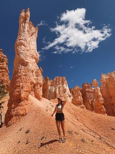 a woman standing on top of a dirt field next to tall rock formations in the desert