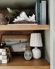 a shelf with books, vases and other items sitting on top of it next to a lamp