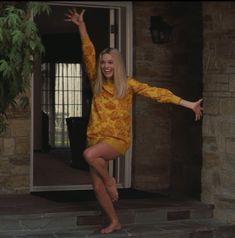 a woman in yellow dress standing on steps with her arms out and legs spread wide