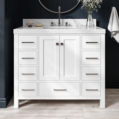 a white bathroom vanity with marble top and drawers under a round mirror over the sink