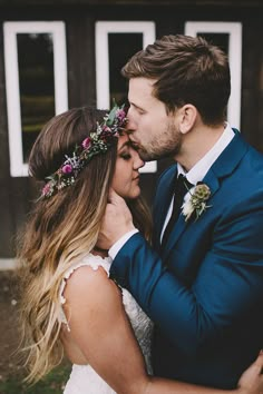 a bride and groom are kissing in front of a barn with flowers on their head