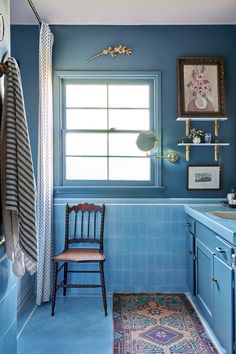 a blue tiled bathroom with a chair in the corner and a rug on the floor