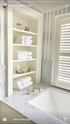 a white bathroom with blue and white wallpaper on the walls, shelving in front of a bathtub