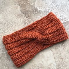 an orange knitted headband with a knot on it sitting on a stone surface