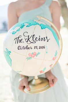 a woman in a white dress holding a globe with the name of her wedding date