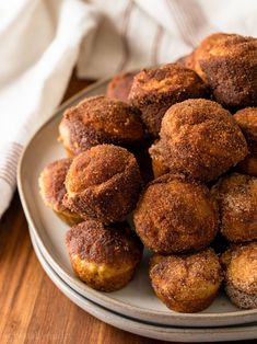 a plate full of sugared donuts on a wooden table next to a napkin