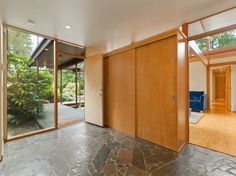 an empty living room with large windows and wood paneling on the walls, along with stone flooring