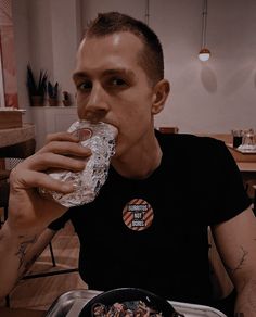 a man sitting at a table eating food and drinking from a plastic bottle in front of him