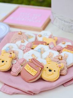 winnie the pooh cookies are sitting on a pink table cloth next to some other items