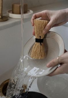 a person is holding a brush over a sink faucet with water running from it