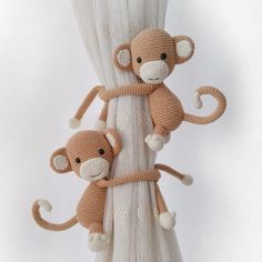 two stuffed monkeys hanging from the side of a white curtain with their arms around each other