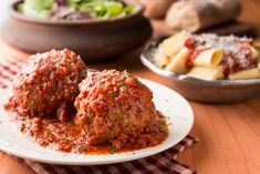 two meatballs covered in marinara sauce on a plate next to pasta and salad