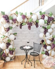 a table and chairs in front of a large balloon arch with grapes hanging from it