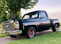 an old black pickup truck parked on the side of a road next to a tree