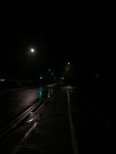 an empty street at night with the lights on and one car driving down it's side