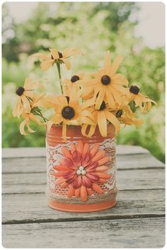 an orange vase with yellow flowers on top of a wooden table