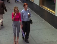 two women walking down the street while one holds an umbrella and looks at her cell phone