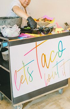 a woman standing behind a sign that says let's taco boutt it