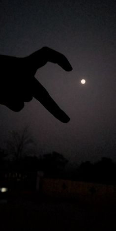 a person's hand pointing at the moon in the night sky