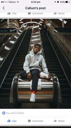 a man sitting on top of an escalator in a white sweatshirt and black pants