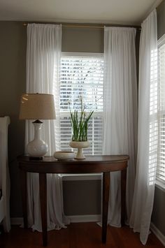 a small table with a lamp on it next to a window covered in white curtains