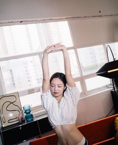 a woman is doing yoga in front of a window with her arms up and hands behind her head