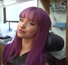 a woman with long purple hair is sitting in a chair and looking at the camera