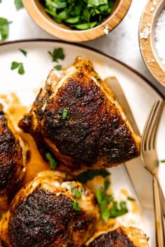 three pieces of meat sitting on top of a white plate next to a bowl of greens