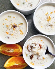 four white bowls filled with food next to sliced oranges and an apple on the side