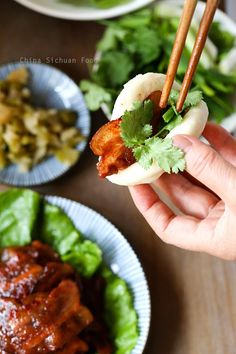 a person holding chopsticks over some food on a plate with lettuce