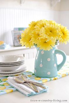 a blue vase filled with yellow flowers sitting on top of a table next to plates and silverware