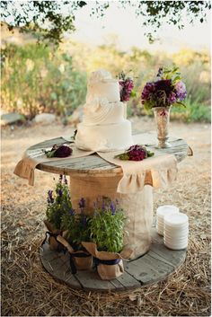 a wedding cake sitting on top of a wooden table covered in flowers and greenery