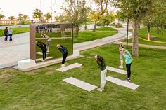 three women doing yoga in front of a large mirror on the grass with their hands up