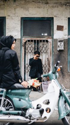 two people standing next to a parked motor scooter in front of a building