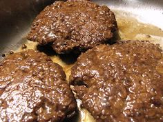 three hamburger patties cooking in a frying pan