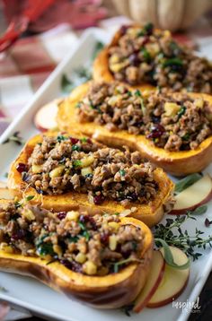 three stuffed sweet potatoes on a white platter with apples and cranberry sauce