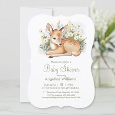 a baby shower card with a deer and daisies on the front, sitting next to a vase of flowers