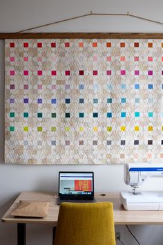 a laptop computer sitting on top of a desk next to a sewing machine and quilt