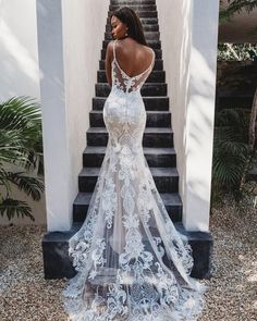 a woman standing in front of some stairs wearing a white wedding dress with sheer sleeves