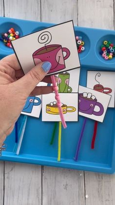 a hand holding a pink pen over some pictures on a blue tray with candy sticks